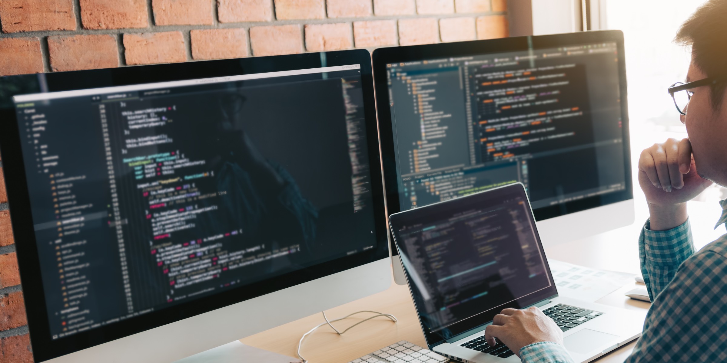 A person working on web development using two monitors and a laptop