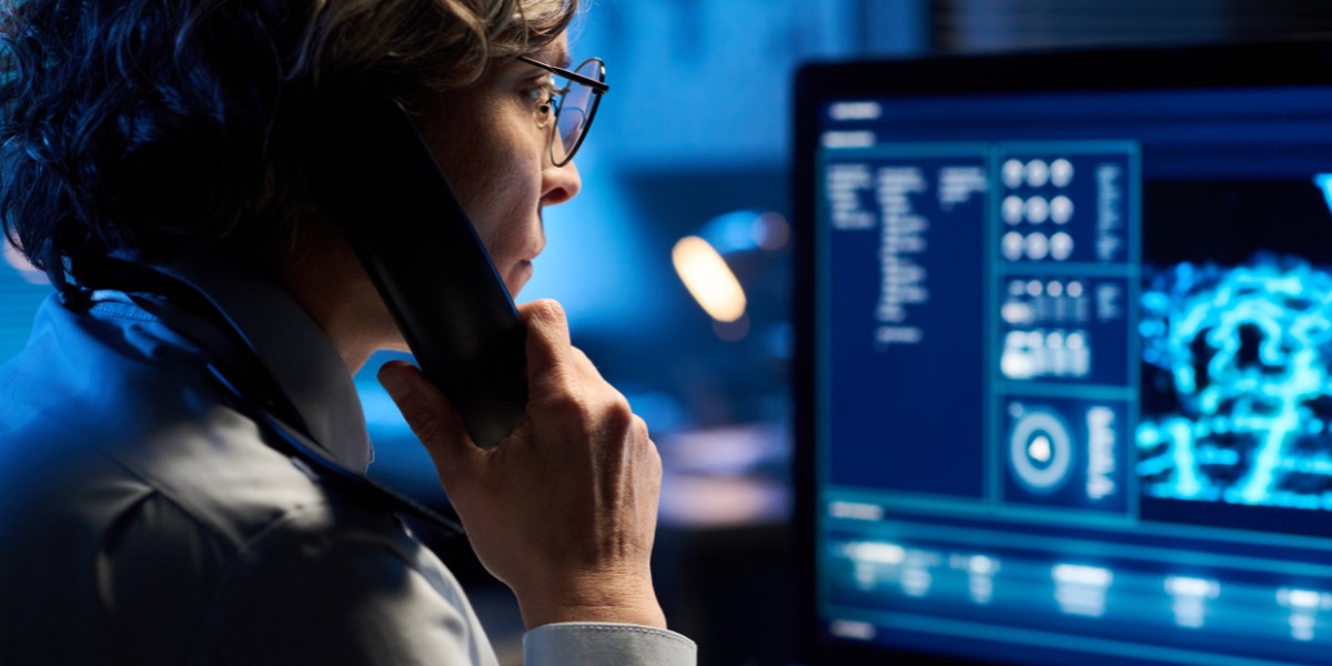 Person sitting at a desk looking at a computer with a phone up to their ear