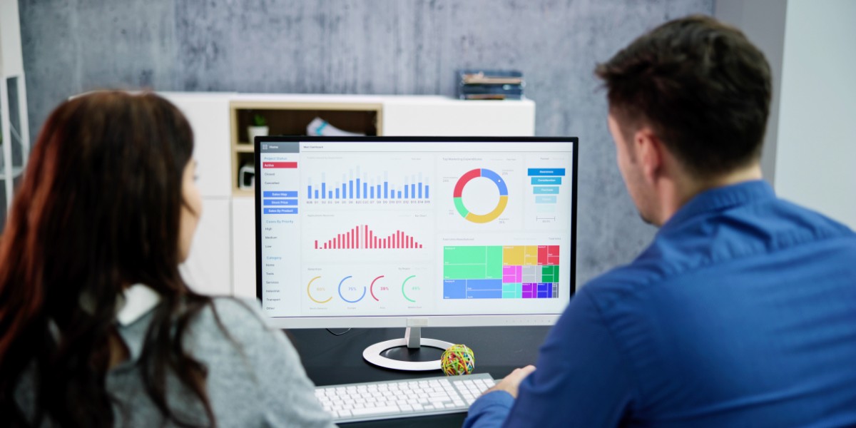 Two people sitting at a desk looking at a computer monitor filled with charts and graphs
