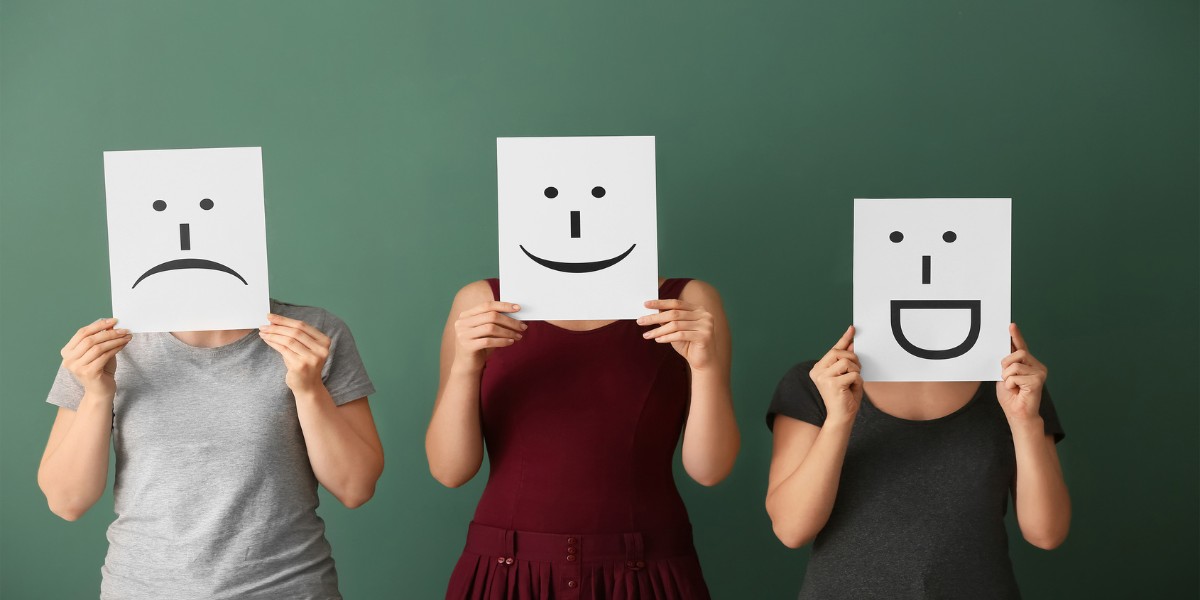 Three people whose faces cannot be seen because they are holding up large cards with emoticons in front of their face representing different emotions such as sad, happy, and joyful