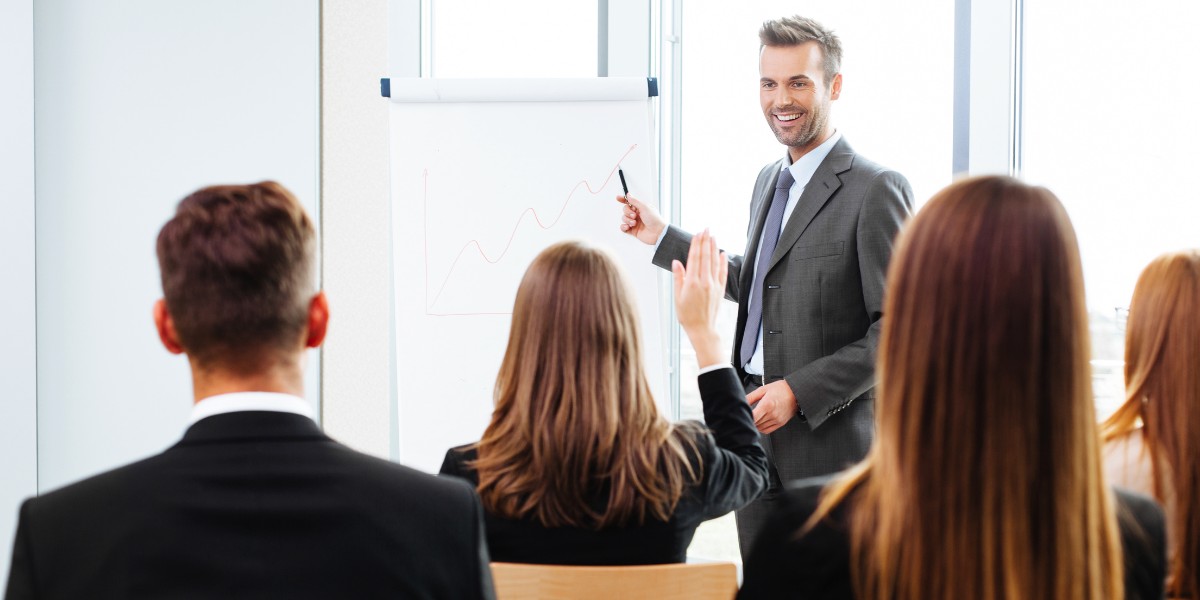 A trainer standing at a flip chart at the front of a classroom bull of business professionals