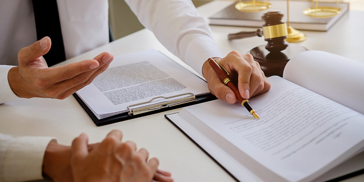 Two professionals sitting at a table reviewing documents in a book and on a clipboard with a gavel and scales of justice off to the side