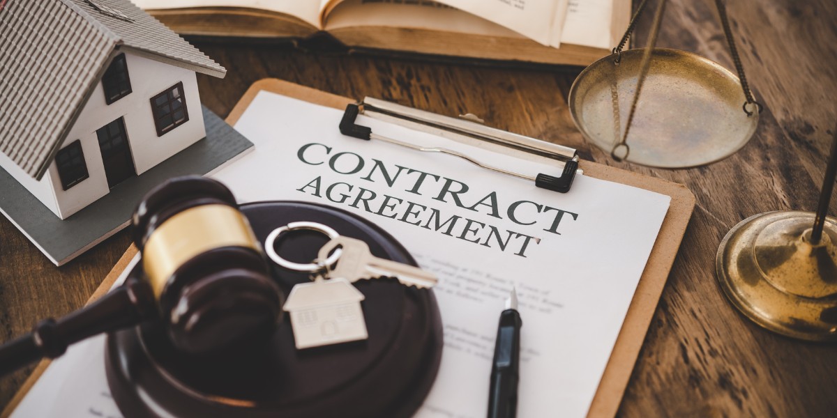 A contract agreement, set of keys, small model house, gavel, and scales of justice arranged on a table