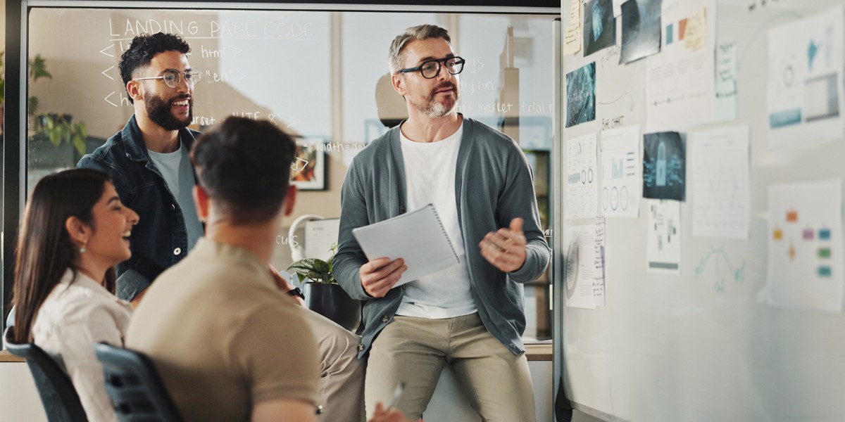 A project team meeting around a white board with charts and papers posted on it