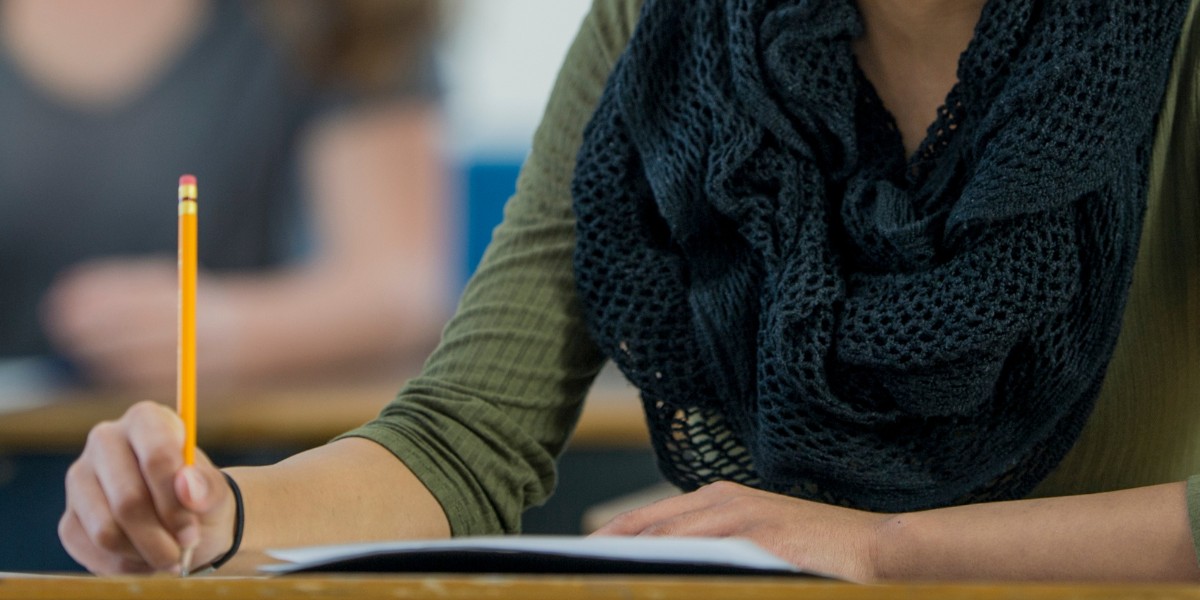 A person sitting in a student style desk in a classroom taking a test